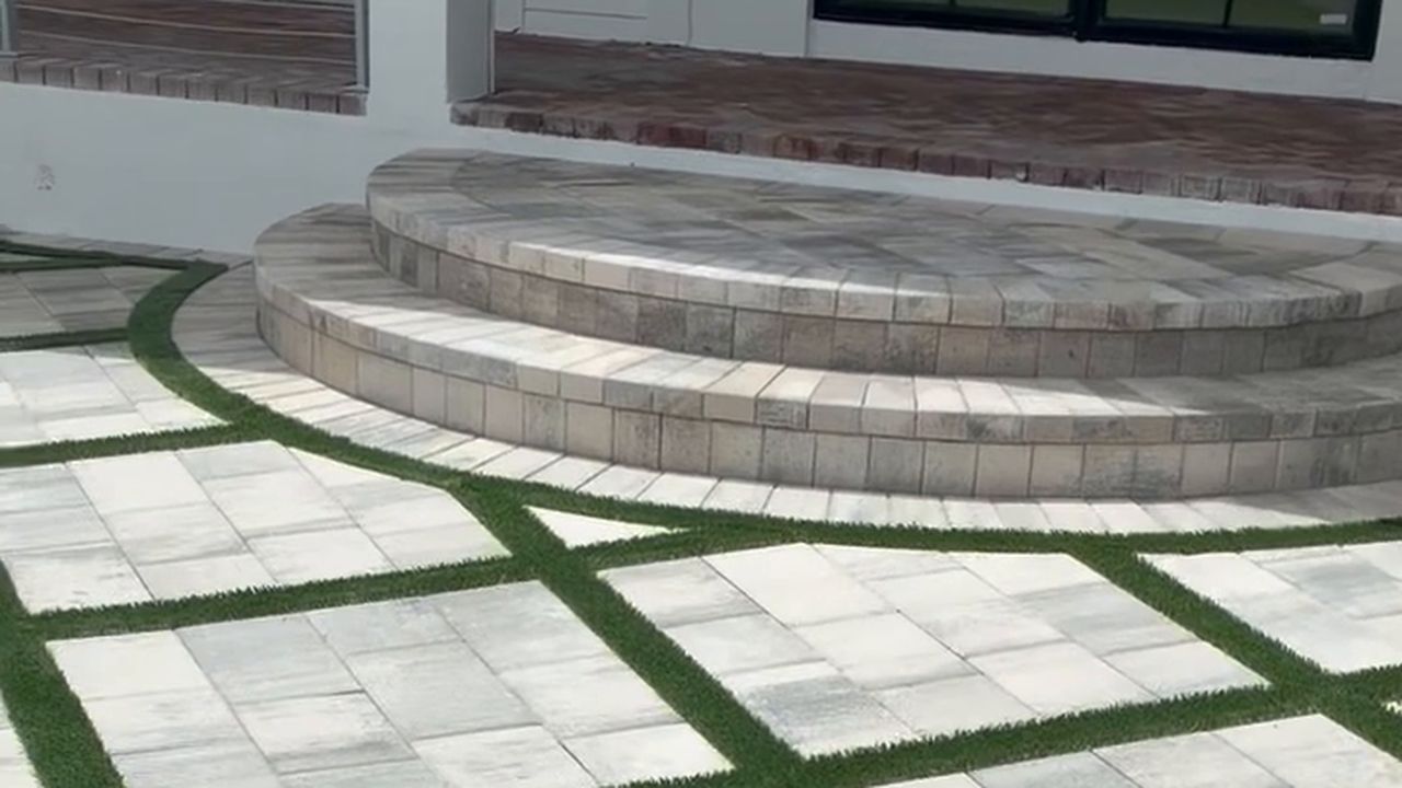 Curved paver steps rising from a light gray paver entry laid in a diamond pattern with green turf joints