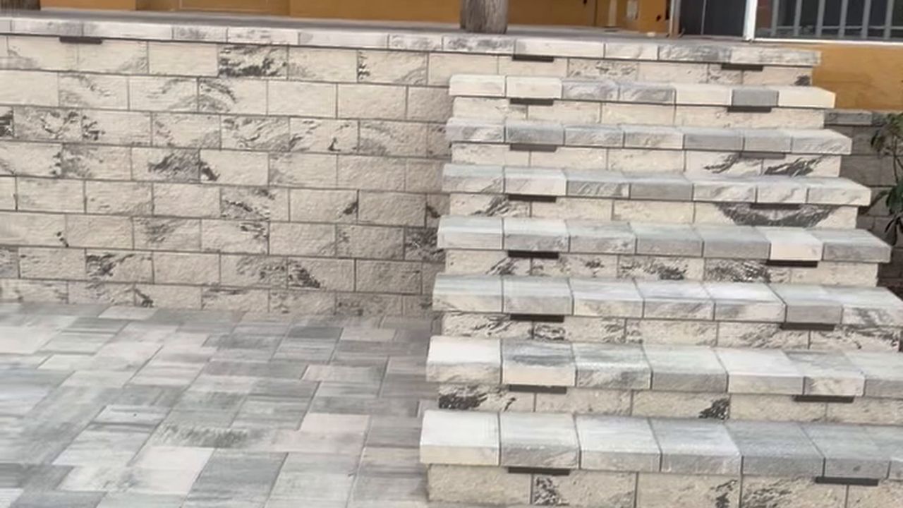 Gray and tan paver patio with stacked stone steps and a stone retaining wall