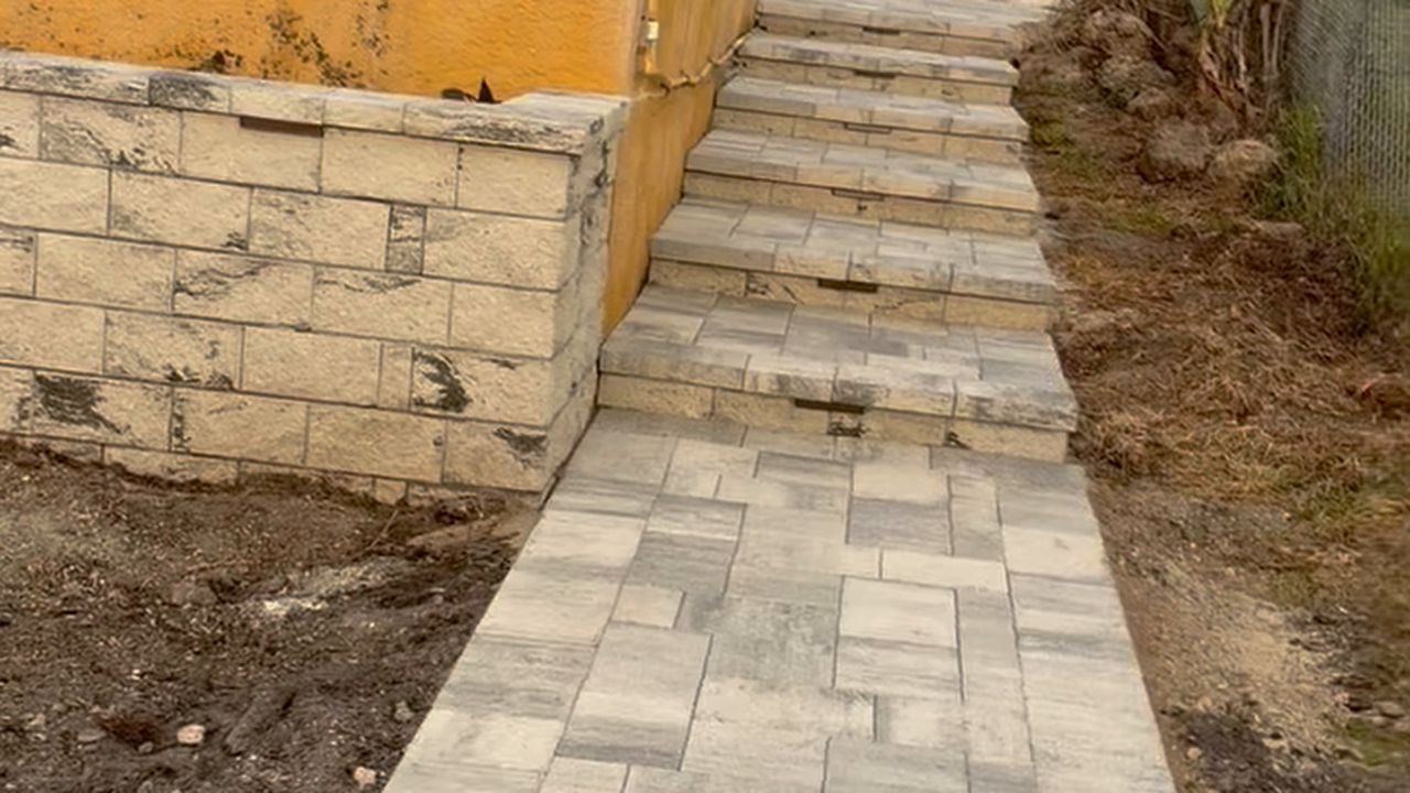 Paver walkway beside a stone retaining wall leading up to stone steps